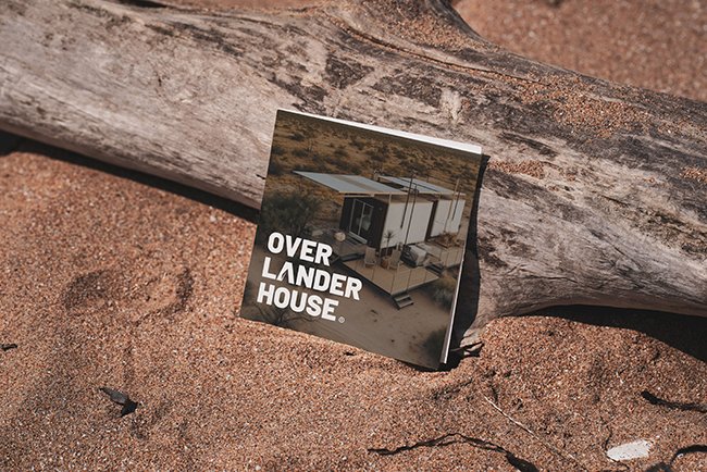 flyer de la marca Overlander House recargada en un tronco y sobre arena